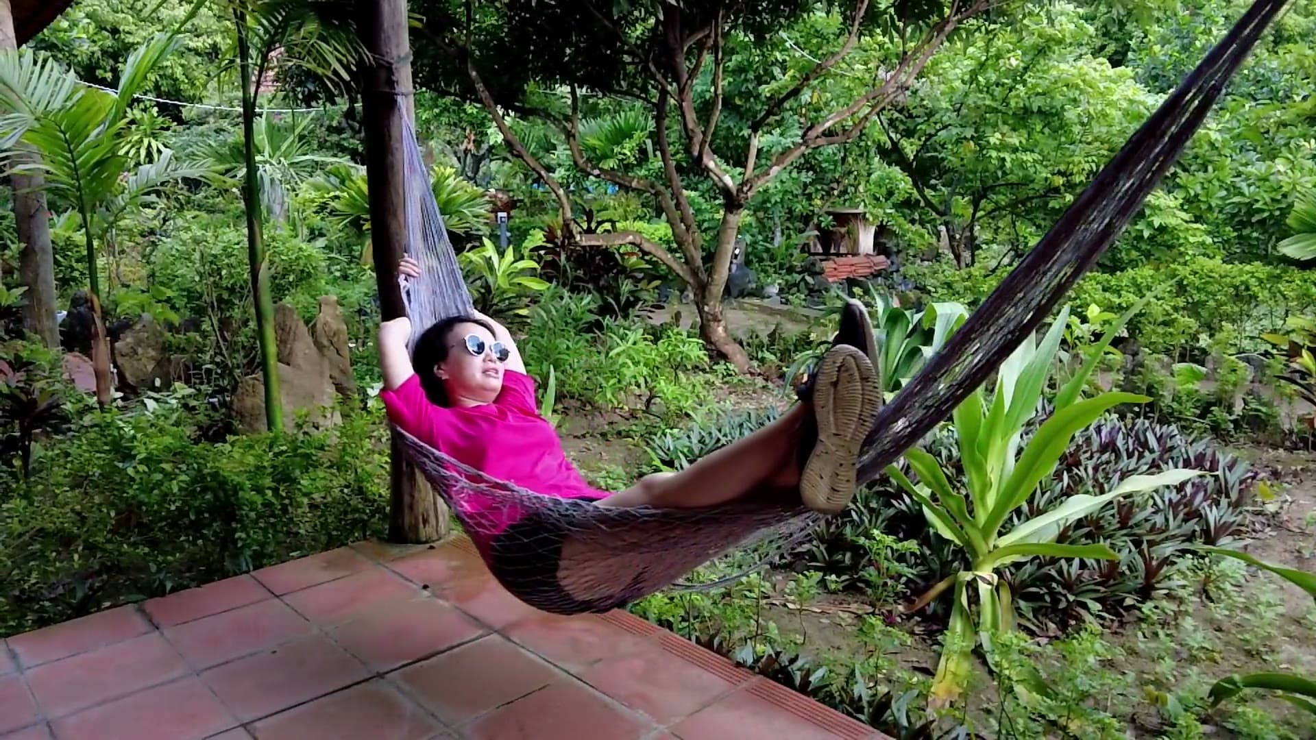 Une personne allongée dans un hamac, au milieu d'un jardin tropical